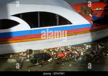 Plastic bottles and other trash floating in Manado River next to wooden boat Stock Photo