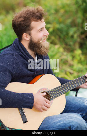 smiling man playing guitar in camping Stock Photo