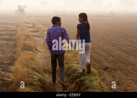 India, Uttar Pradesh, Agra, brother and sister holding hands walking in field Stock Photo