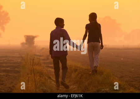 India, Uttar Pradesh, Agra, brother and sister holding hands walking in field Stock Photo