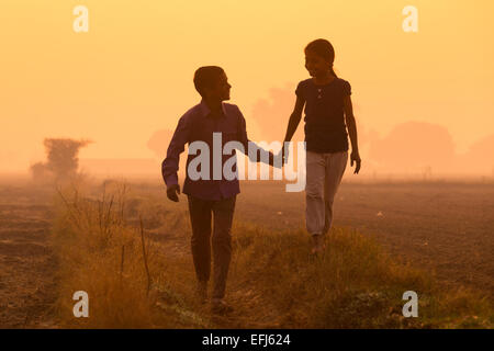 India, Uttar Pradesh, Agra, brother and sister holding hands walking in field Stock Photo