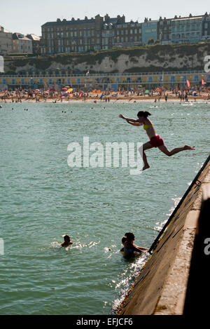 Girl jumps of the end of the pier into the sea at Broardstairs, Kent. While other swimmers are in the water. On a summer day. Stock Photo