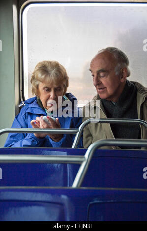 Vertical portrait of an elderly couple sitting together on a bus using a smartphone. Stock Photo