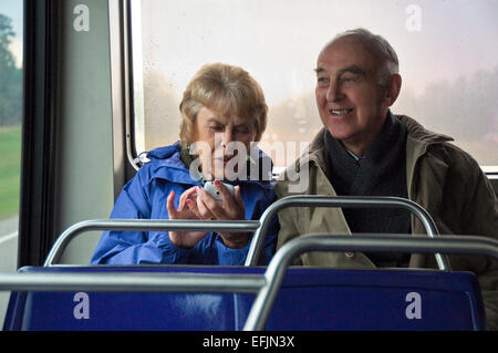 Horizontal portrait of an elderly couple sitting together on a bus using a smart phone laughing. Stock Photo