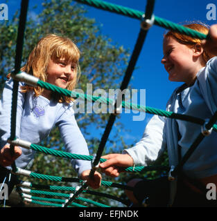 Two girls having fun playing on climbing frame in sunshine in the park, Llandeilo Carmarthenshire Wales UK   KATHY DEWITT Stock Photo