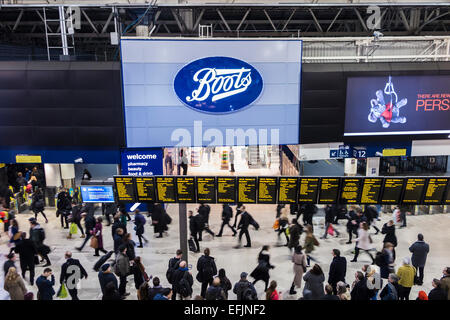 Boots shop sign and logo at London Waterloo Station concourse, crowded with early evening commuters walking under the departure boards Stock Photo