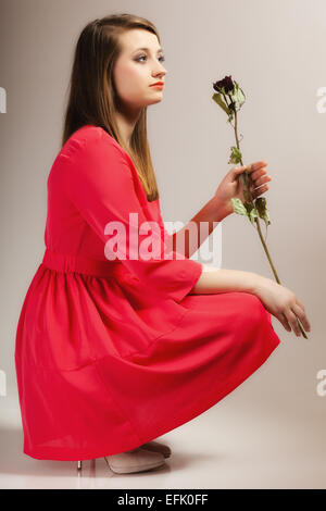 Beautiful fashion woman in full length teen girl in red gown with dry rose on gray background Stock Photo