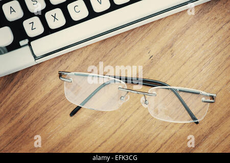 Top view of old fashioned typewriter from the 1970s and modern eyeglasses on wooden table. Stock Photo