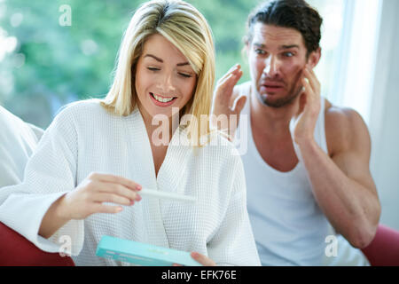 Happy girl finding out she is pregnant with upset man in background Stock Photo