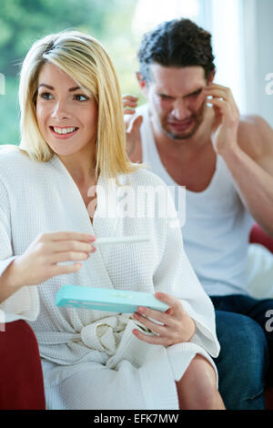 Happy girl finding out she is pregnant with upset man in background Stock Photo