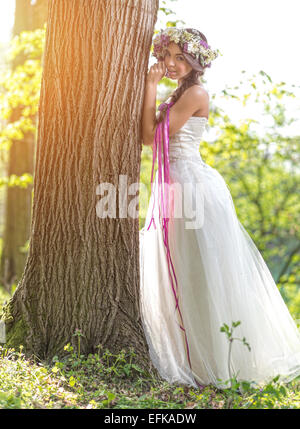 Beautiful bride , flower tiara on her head , relying on the tree