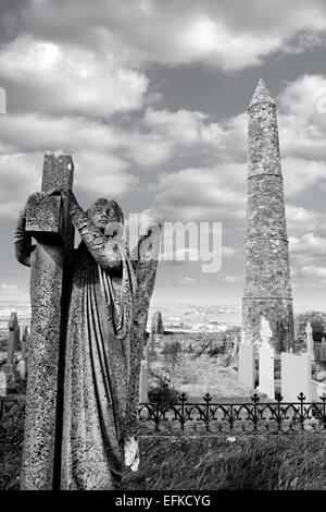 Angel statue before an Ancient round tower and celtic graveyard with cathedral in Ardmore county Waterford, Ireland Stock Photo