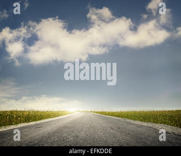 Wide road and green meadow at blue cloudy sky background Stock Photo