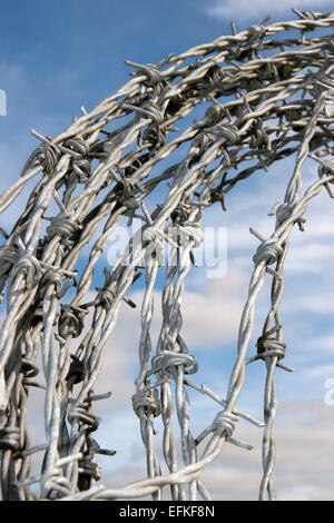 a coil of dangerous barbed wire with a blue cloudy sky background Stock Photo