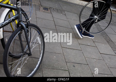 A person carries a bicycle wheel, minus its tyre, past locked up bikes in central London. Stock Photo
