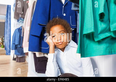 African boy with hand on cheek sits under hangers Stock Photo