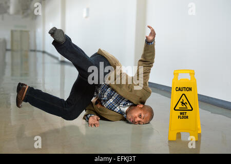 African American businessman falling on wet floor in office Stock Photo