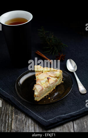 Slice of apple pie with dark tall cup of tea on dark napkin, black background Stock Photo