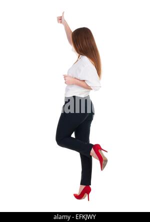 back view of standing young redhead business woman showing thumb up. beautiful businesswoman in black suit gesturing ok sign. Rear view people collection. backside view of person. Isolated over white background Stock Photo