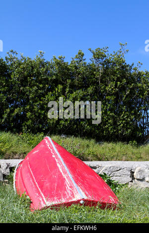 Upturned red rowing boat leaning against footpath, Isles of Scilly, UK
