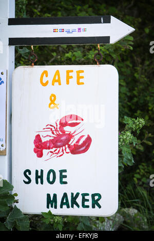 Handmade sign for cafe and shoe maker hanging from direction arrow, Isles of Scilly, Uk Stock Photo