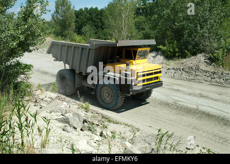 Yellow dump truck driving on a road in a stone quarry Stock Photo