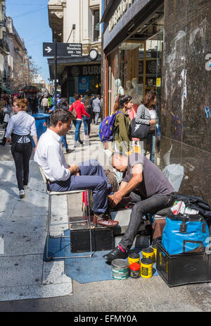 Local man shoe shining for a customer in Calle Florida (Florida Street), one of the main shopping streets in downtown Buenos Aires on a sunny day Stock Photo