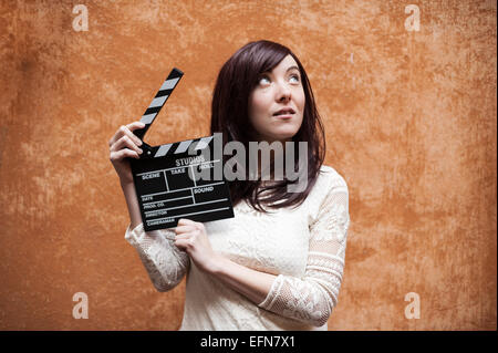 Young woman in 70s hippie style closeup with clapperboard, outdoor orange wall background Stock Photo