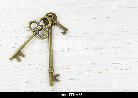 Three brass keys on a white distressed wood background. Copy space. Stock Photo