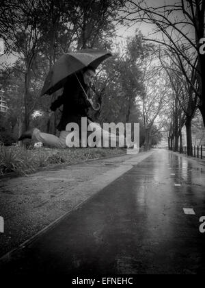 Conceptual black and white photo of a man jumping with an opened umbrella in the rain. Stock Photo