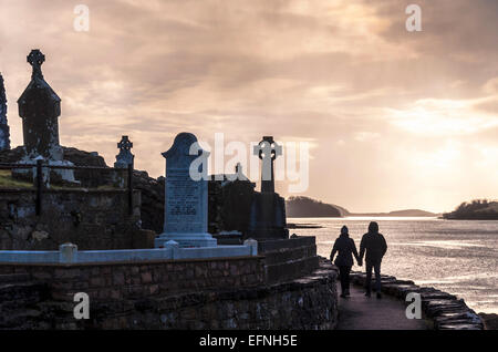 A couple walk by Old Abbey Cemetery and Donegal Bay in Donegal Town County Donegal Ireland Stock Photo