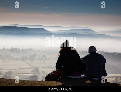 Two hikers sit on Ragleth Hill and gaze across a misty South Shropshire, England Stock Photo
