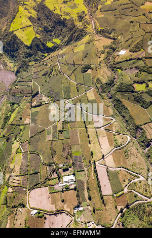 An aerial photograph captures a patchwork of terraced agricultural fields carved into a mountainous valley. The fields vary in color from bright green to brown, indicating different crops or stages Stock Photo