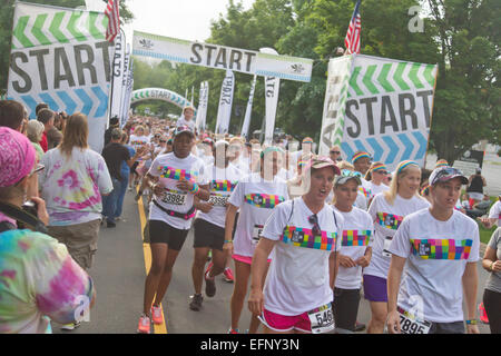 Color Run participants wearing colorful t-shirts and headbands enthusiastically take off walking from the starting line Stock Photo