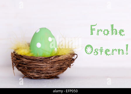 One GreenDotted Easter Eggs In Easter Basket Or Nest On White Wooden Background With German Text Frohe Ostern Means Happy Easter Stock Photo