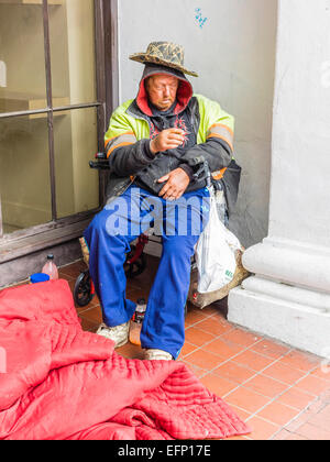 A homeless man smokes a cigarette in an enclosure outside in the front of a store on State Street in Santa Barbara, California. Stock Photo