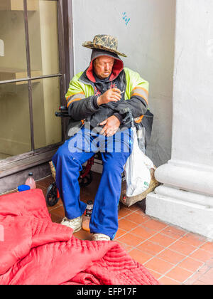 A homeless man smokes a cigarette in an enclosure outside in the front of a store on State Street in Santa Barbara, California. Stock Photo