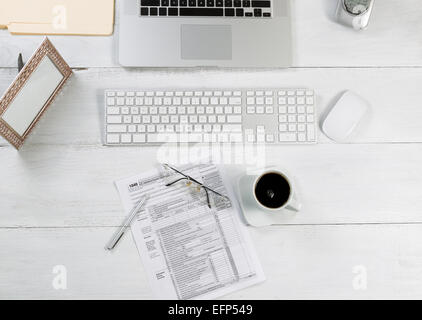 Top view angle of office desktop consisting of laptop, keyboard, pens, mouse, picture frame, phone, coffee, reading glasses, tax Stock Photo