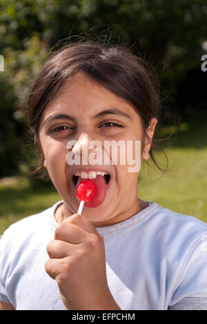 Happy child young girl outside sucking lollipop sweet on a paper handle need to look after teeth due sugar Stock Photo