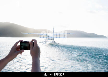 Womans hands photographing seaplane taking off from Long Island, Whitsunday Islands, Queensland, Australia Stock Photo