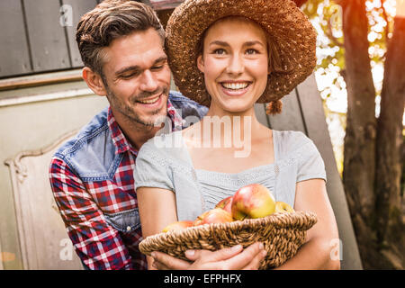 Mid adult man embracing young woman, young woman holding basket of apples Stock Photo