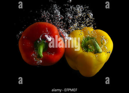 Red and yellow peppers in water with air bubbles. Photo on black background. Stock Photo