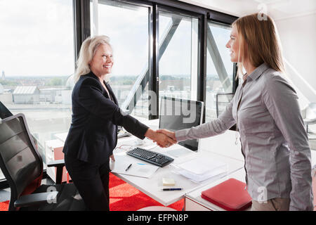 Two women shaking hands in office Stock Photo