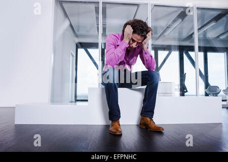 Mature man sitting on podium with head in hands Stock Photo