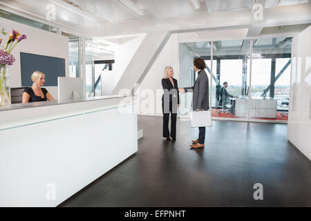Woman shaking hands with visitor at reception Stock Photo