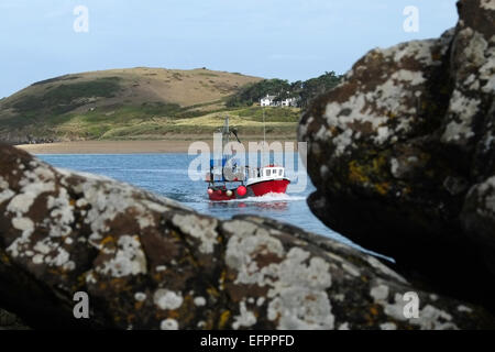 a small red fishing boat returning to port seen through coastal rocks Stock Photo