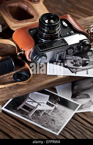 Old rangefinder camera and black-and-white photos on the old wooden table. Stock Photo