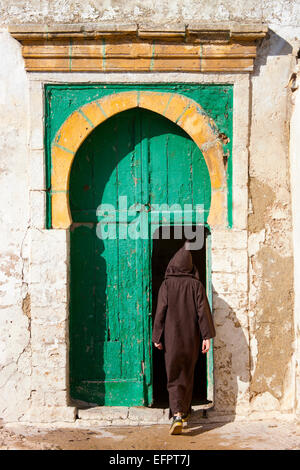 Rear view of man wearing traditional clothing stepping into door, Essaouira, Morocco Stock Photo