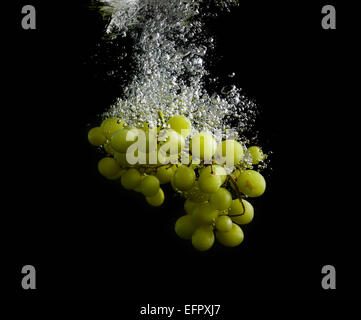 Green grapes fall into the water with air bubbles. Photo on black background. Stock Photo