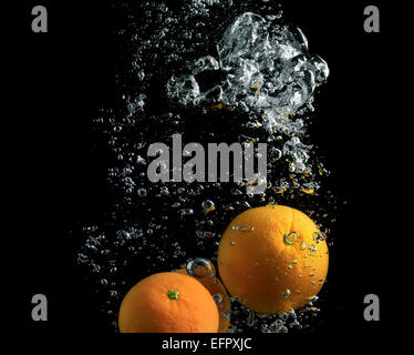 Oranges falling in water with air bubbles on a black background. Stock Photo